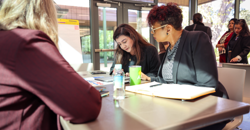 Three women sit at a table in discussion, reviewing documents.