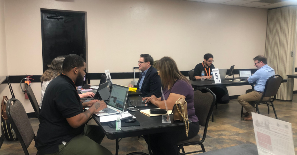 Job seekers being interviewed at tables with laptops and documents in a conference room setting.
