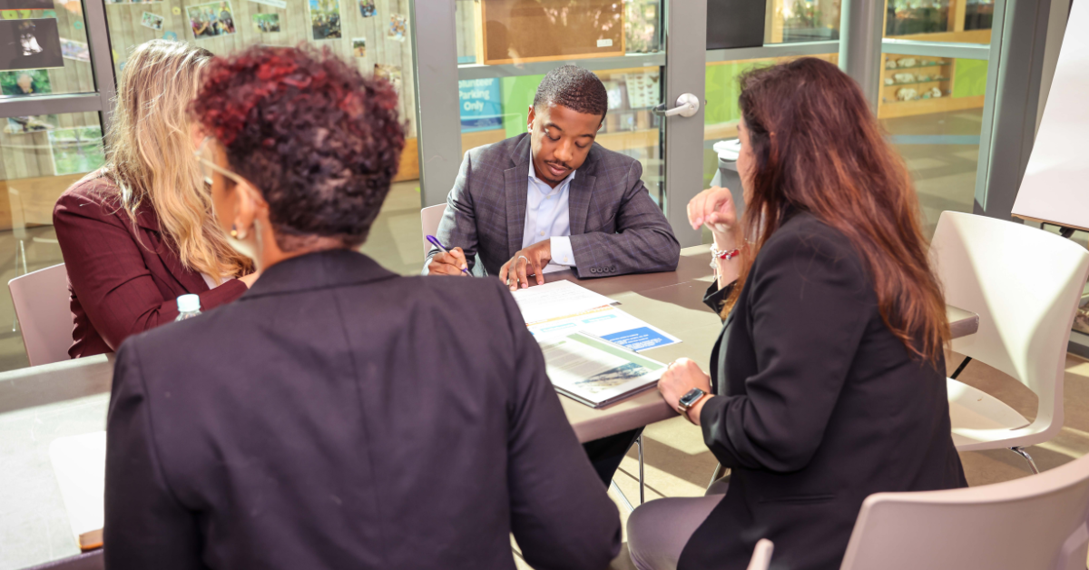 A group of people wearing formal clothes seated at a table in an office.
