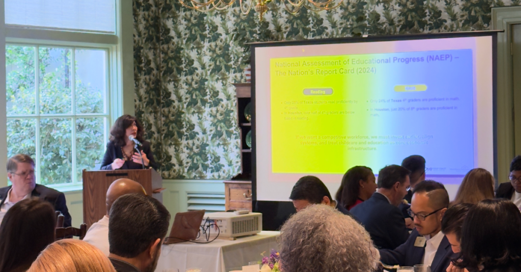 Juliet Stipeche speaks at a podium in a formal setting, with a large slide projected behind her titled "National Assessment of Educational Progress (NAEP).