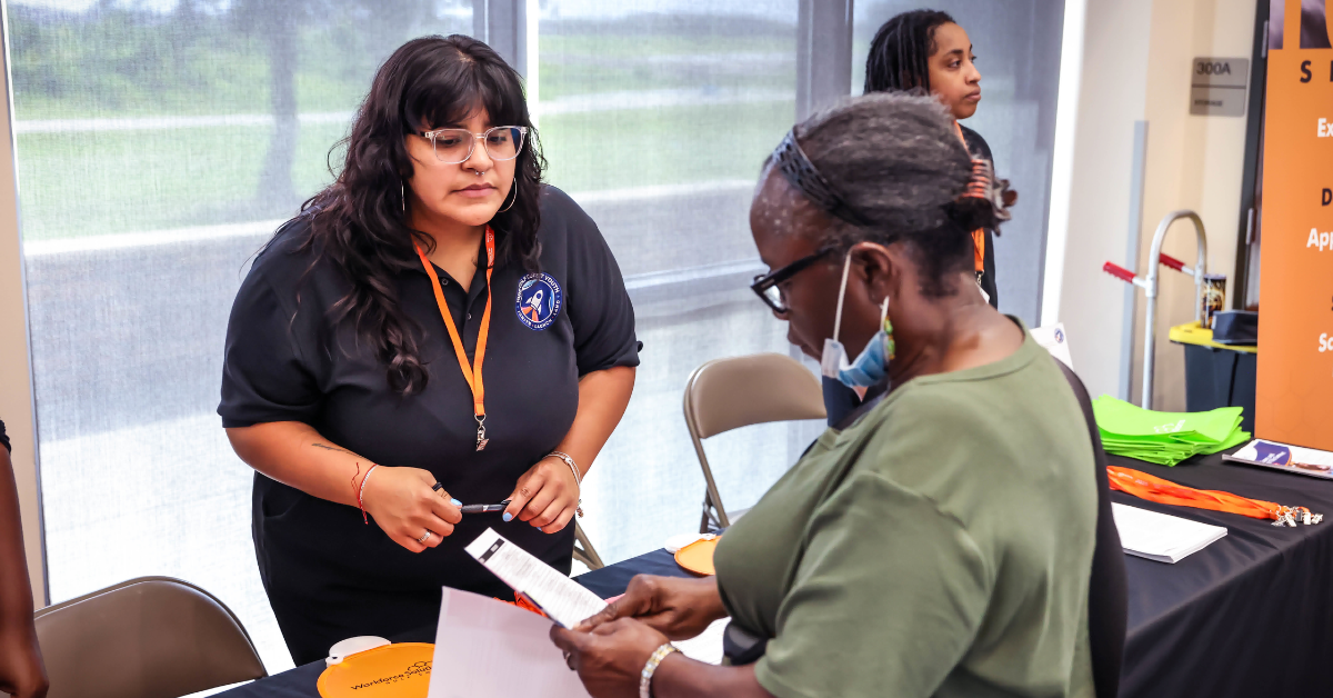 A Workforce Solutions staff member assists another woman at a table during an event.