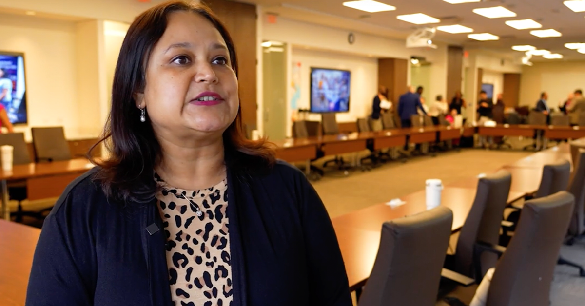 Mou Sarkar, board member, stands in a conference room. The room is filled with long tables and chairs.