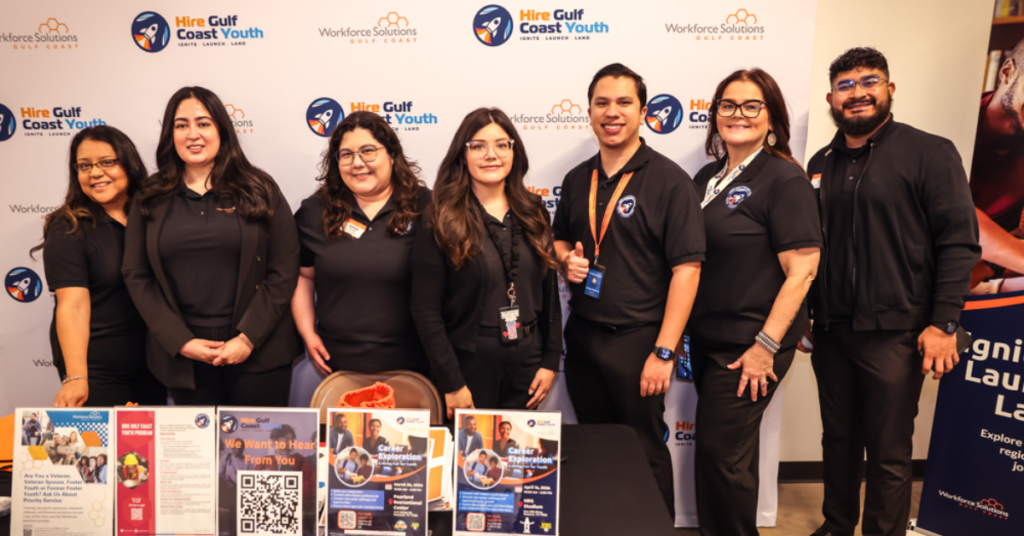 Seven Hire Gulf Coast Youth staff members stand together, smiling at the camera, all dressed in black uniforms.