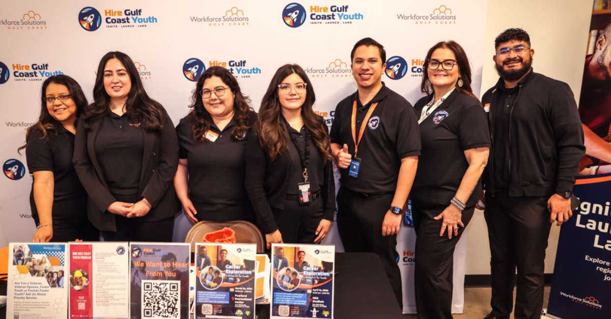 Seven Hire Gulf Coast Youth staff members stand together, smiling at the camera, all dressed in black uniforms.