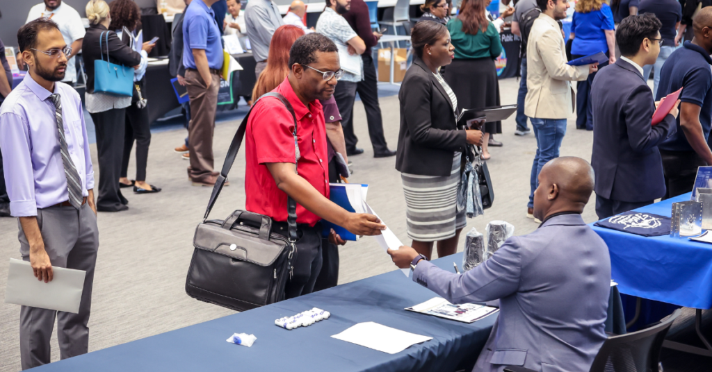 Two men shake hands at a job fair, representing networking and the pursuit of career opportunities in a professional setting.