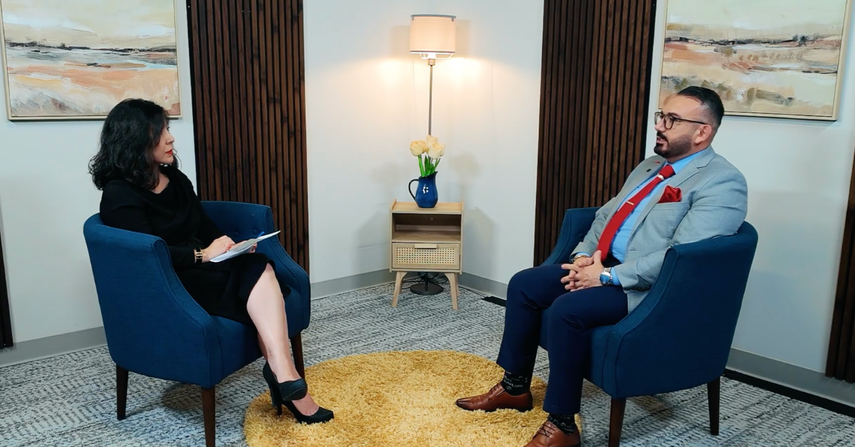 Podcast Episode Juliet Stipeche and Crosby Brito sit facing each other in blue chairs during a formal interview.