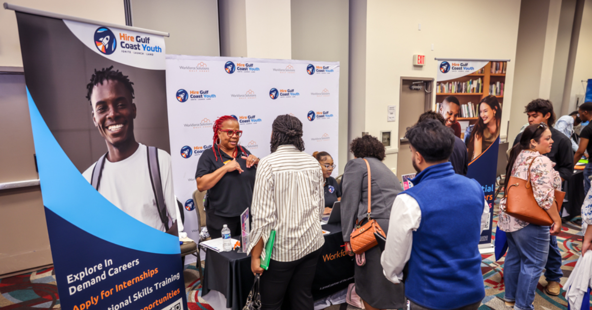 A career fair scene with people interacting at a "Hire Gulf Coast Youth" booth. A banner with a smiling individual promotes career opportunities.