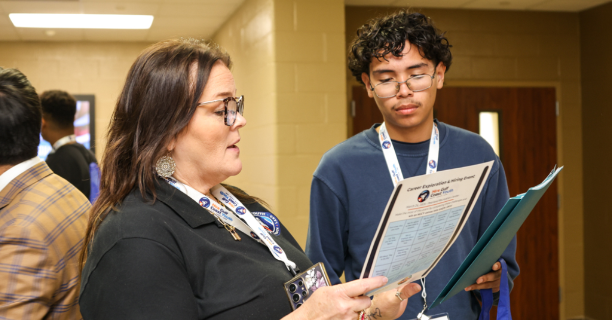 A woman and a young man stand in a hallway, both focused on a paper the woman is holding. They appear to be in a discussion, conveying a collaborative tone.