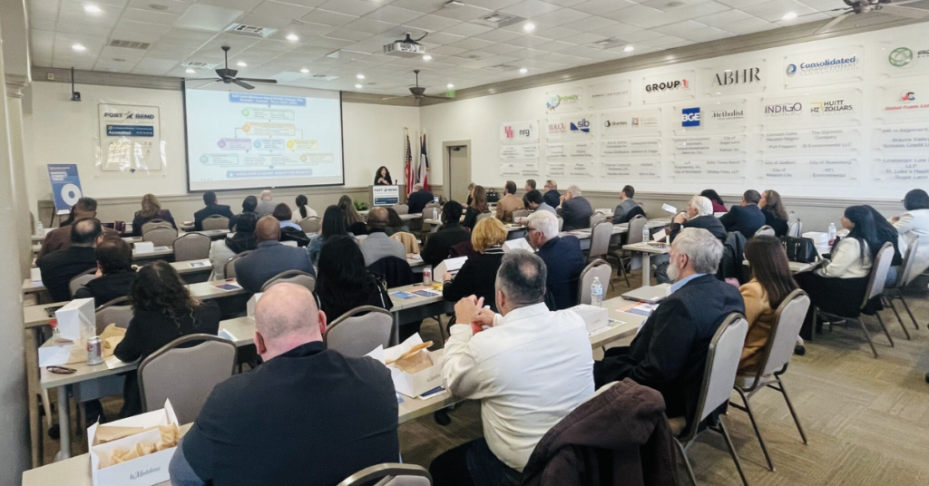 A crowded room filled with tables and chairs. Everyone is listening to the speaker giving a presentation on the workforce.
