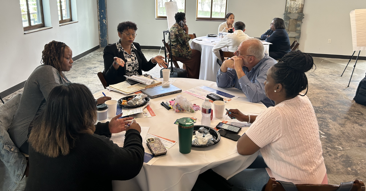 Texas Gulf Coast Workforce Summit—Education A diverse group of people engaged in discussion around a round table in a conference room.