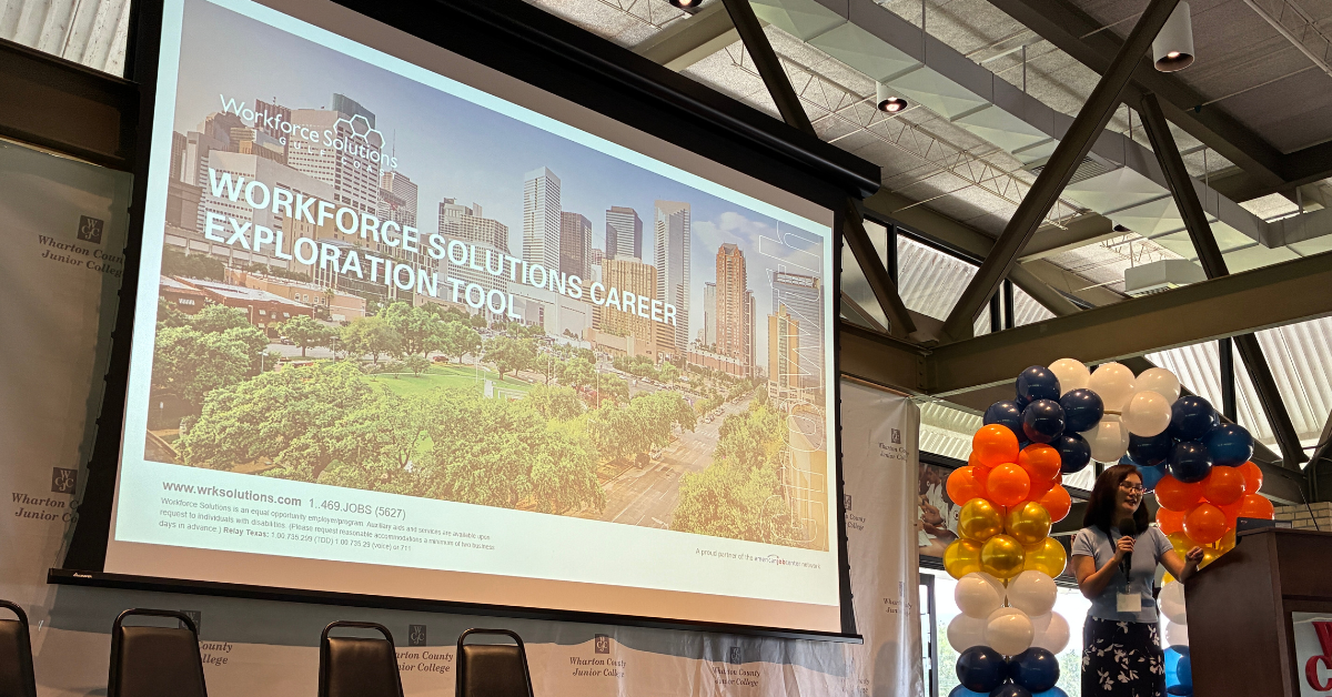 Gulf Coast Workforce Summit A woman speaks at a podium near a colorful balloon arch. A large screen displays "Workforce Solutions Career Exploration Tool" against a cityscape background.