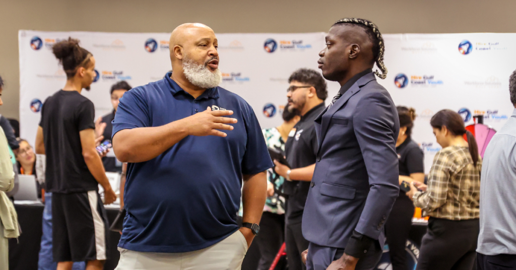 A man with a beard in a blue polo shirt talks to a man at the Sunnyside Job Fair.