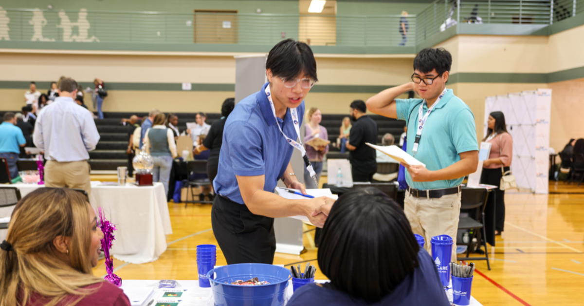 Youth Job Fair A job fair in a gym; a man in a blue shirt shakes hands with a seated woman at a table.
