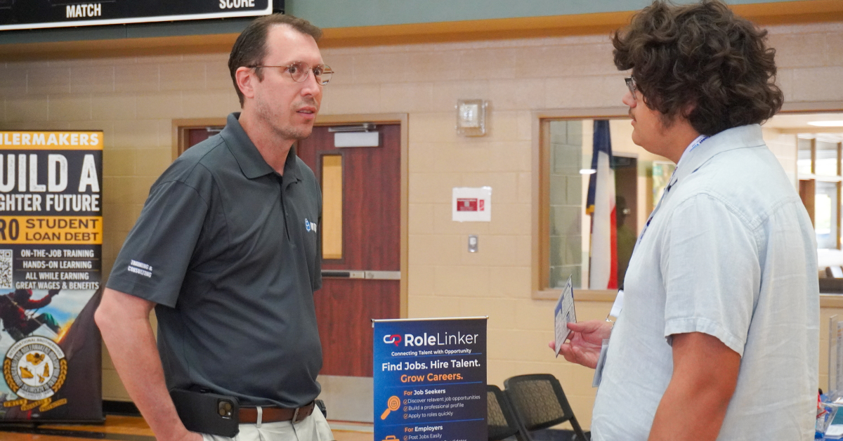 Job seeker speaks with an employer representative at a career fair information booth.