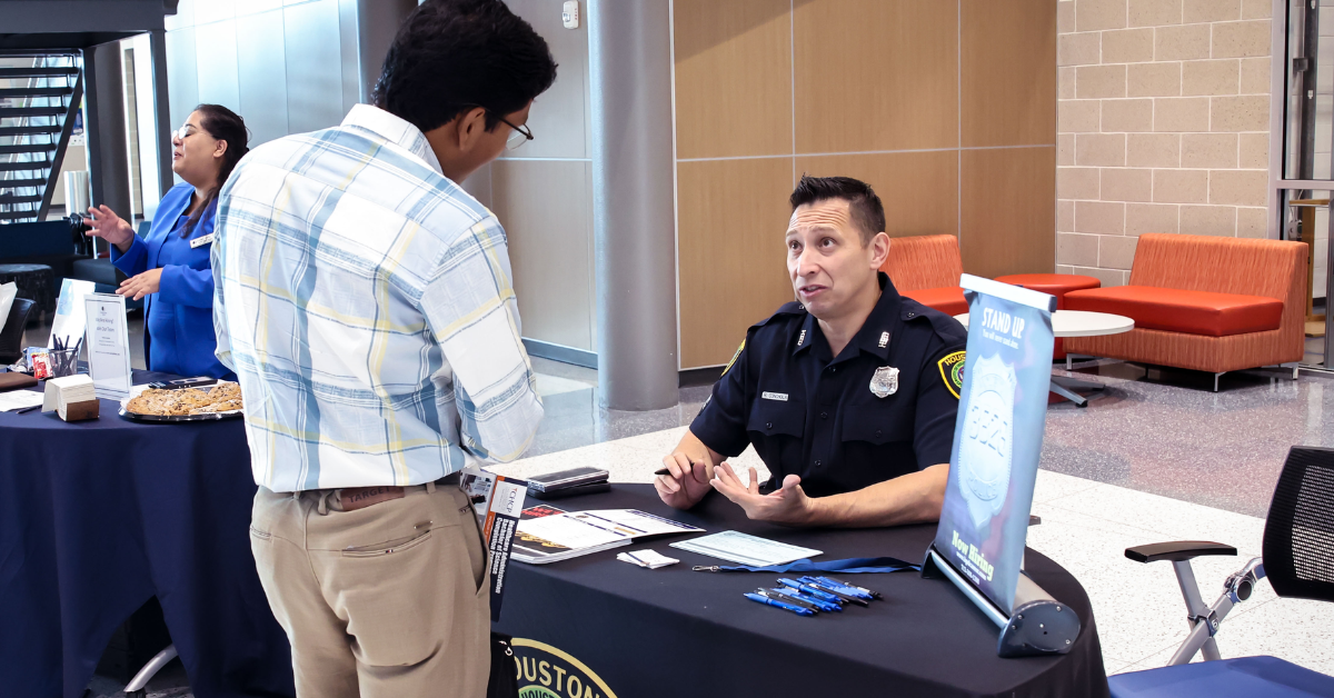 Police officer speaks with a job seeker at a public safety career information booth.