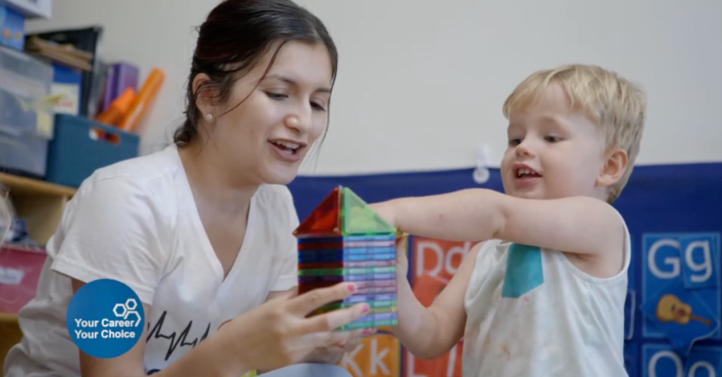 Childcare professional plays with a young child using colorful magnetic tiles in an early learning classroom.