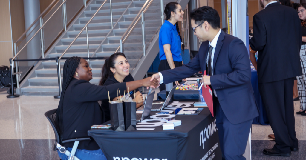 A job seeker shakes hands with an employer at a hiring event while discussing career opportunities.
