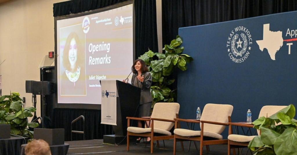 Juliet Stipeche delivers opening remarks at the 10th Annual ApprenticeshipTexas Conference as attendees watch from the audience.