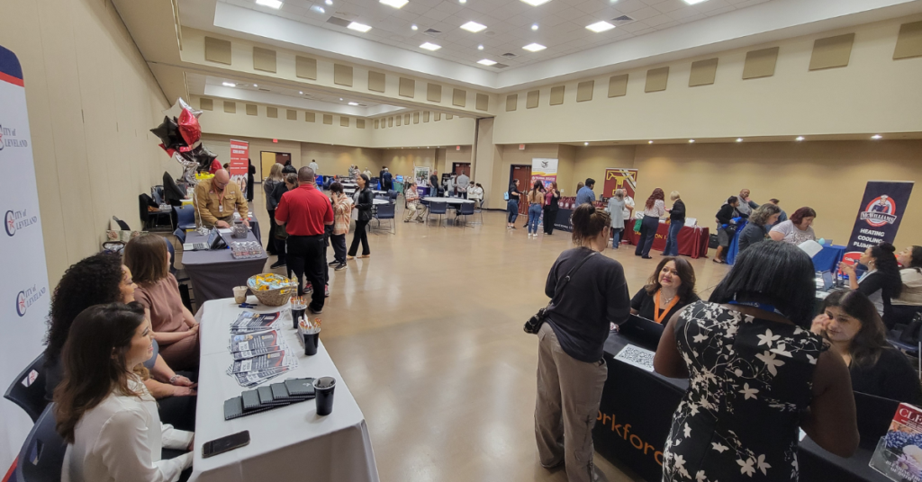 Job seekers and employers connect at a community hiring event, with attendees visiting informational booths, speaking with staff, and exploring employment opportunities throughout a large event hall.