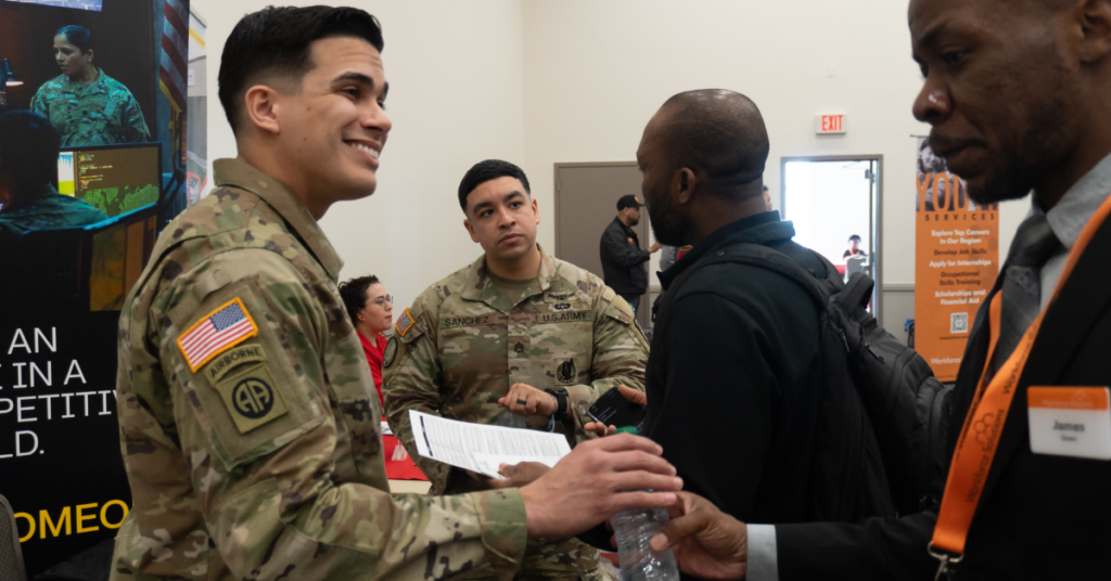 U.S. Army service members in uniform engage in conversation with attendees and employers during a veterans hiring event, sharing information and exploring career opportunities.